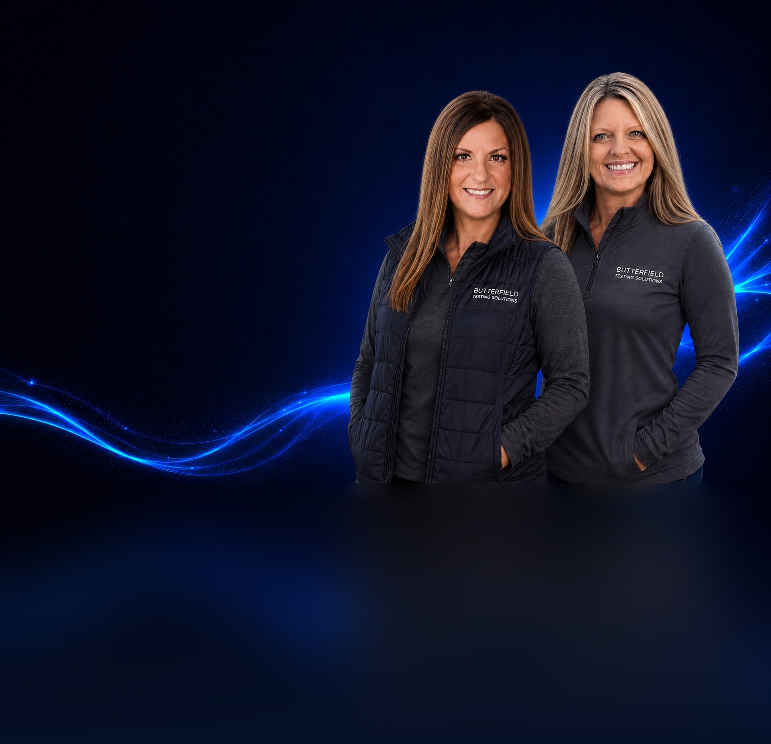 Two Butterfield Testing Solutions team members in branded jackets smiling against a navy background